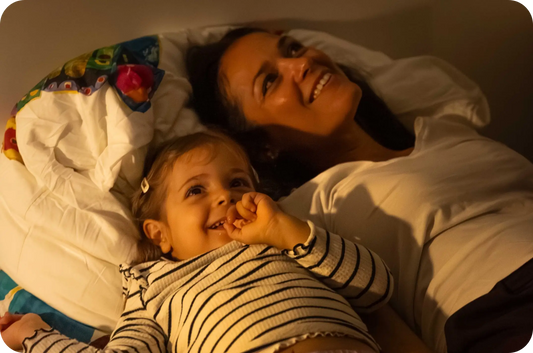 Mutter und Kind liegen eingekuschelt im Bett und bestaunen die BiMA Lichterwelten.