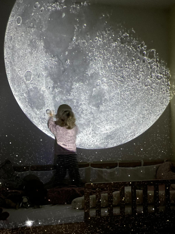 Kleines Mädchen spielt mit der BiMA Lichterwelt Mondlandschaft an der Wand.